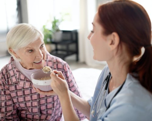 Caring nurse feeding aged woman in the morning