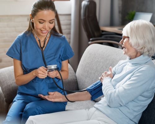 Female nurse checking blood pressure of senior woman at home